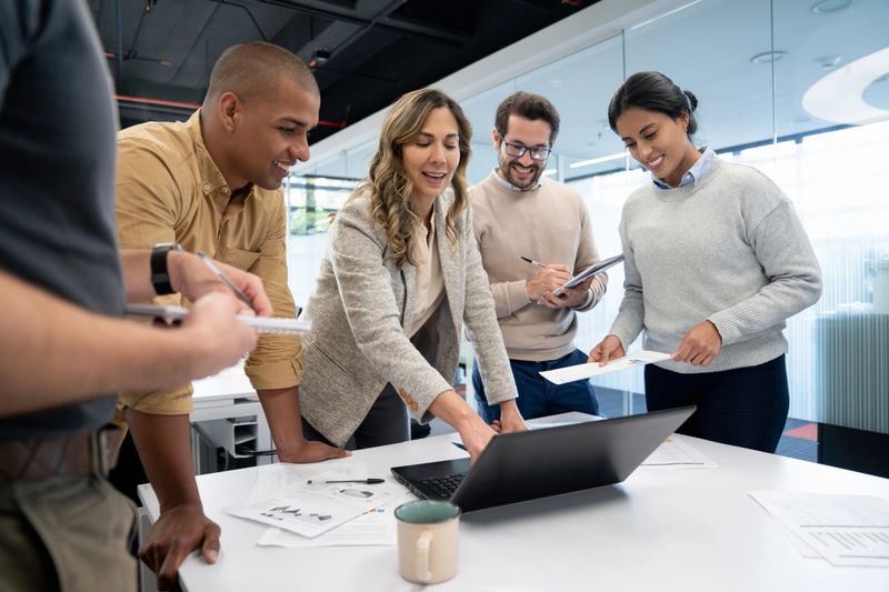 Successful Latin American woman talking to her team in a business meeting at the office and pointing at a laptop