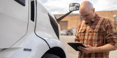 A man inspects a white truck using a tablet outdoors.