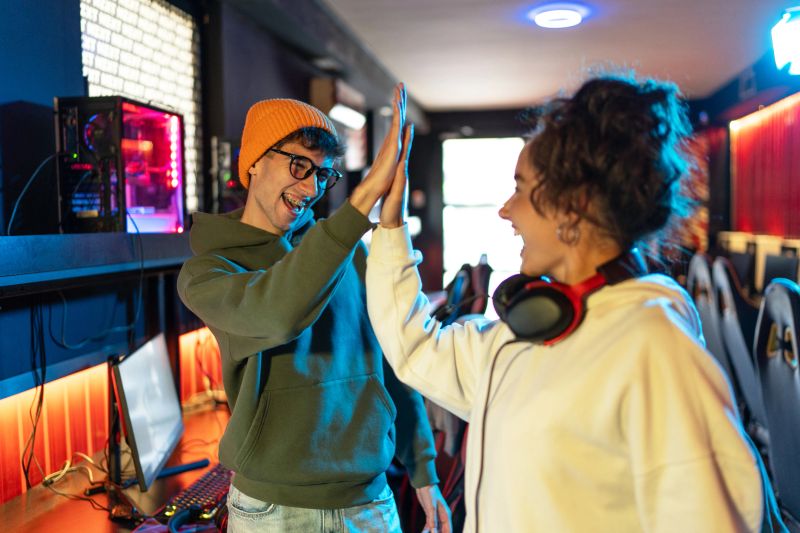 Two young adult gamers celebrating their victory with a high five, enjoying the thrill of winning an online video game tournament at a vibrant gaming center filled with colorful neon lights