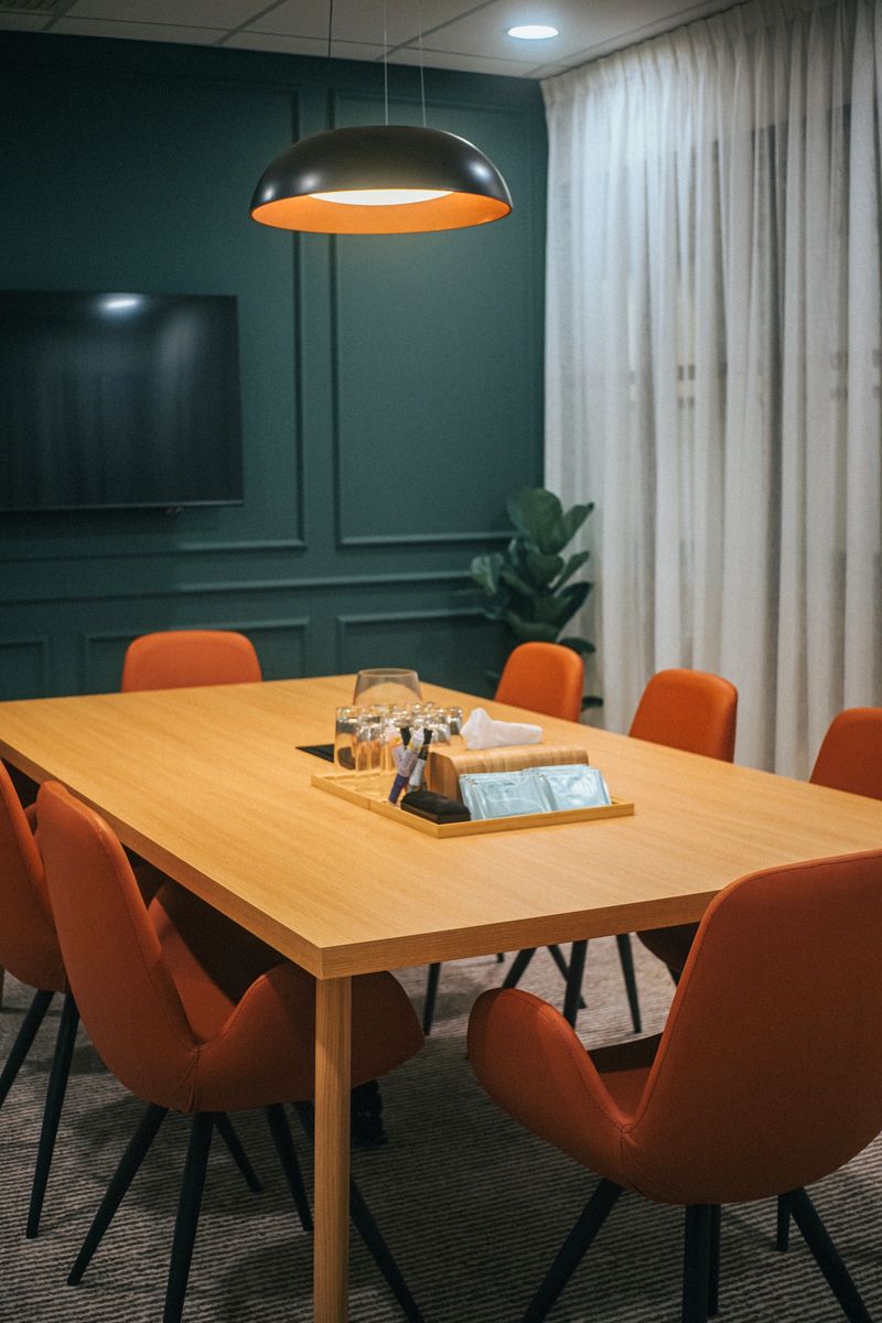contemporary office meeting room with a rectangular wooden table, orange chairs, pendant light, and a wall-mounted TV, designed for collaboration and workplace culture, Kuala Lumpur.