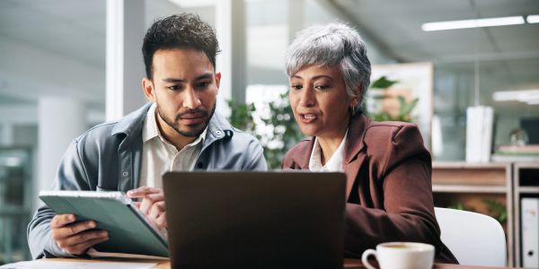 Two coworkers discussing work using a laptop and tablet.