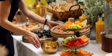 Person serving food from a buffet with fresh vegetables and juice.