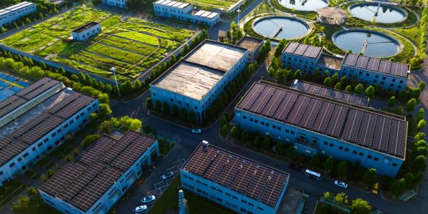 Aerial view of an industrial complex with solar panels and green fields.