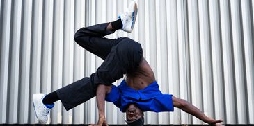Man performing an impressive breakdance move against a metal wall.
