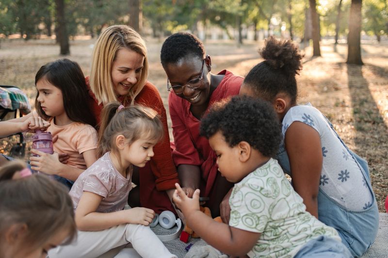 Two teachers playing with a group of preschool children in a park