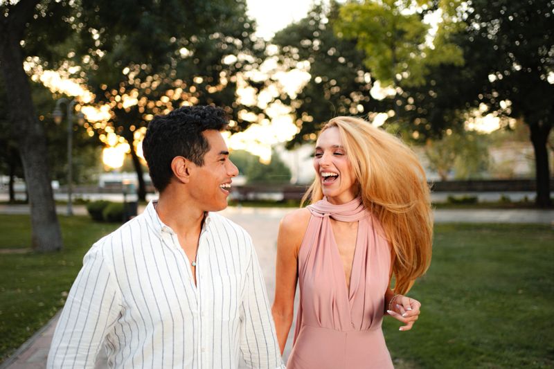 Two friends walk hand in hand, sharing laughter as golden sunlight envelops the park.