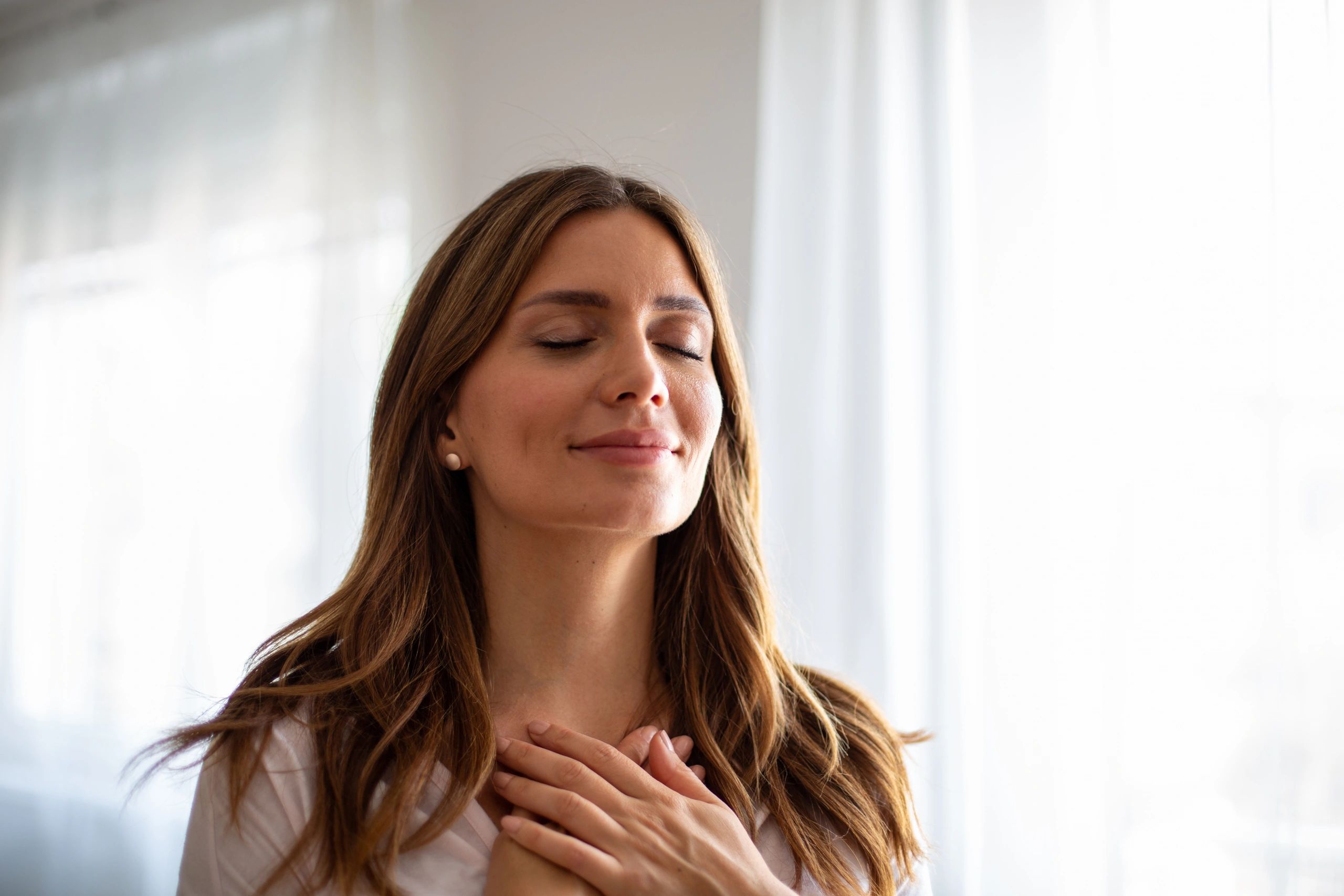 A woman with closed eyes and hands on her chest, feeling grateful.