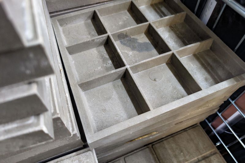 Gray molds with multiple compartments are neatly stacked in a workshop. They are designed for industrial purposes, highlighting efficient organization and space utilization.