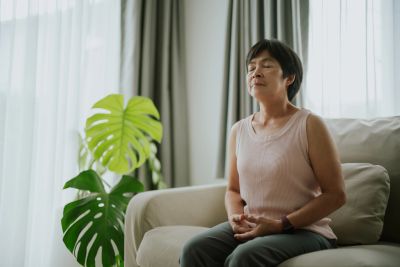 A middle-aged woman meditates peacefully on a sofa.