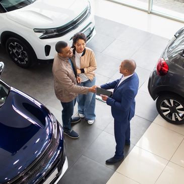 Couple shaking hands with a car salesman inside a showroom.
