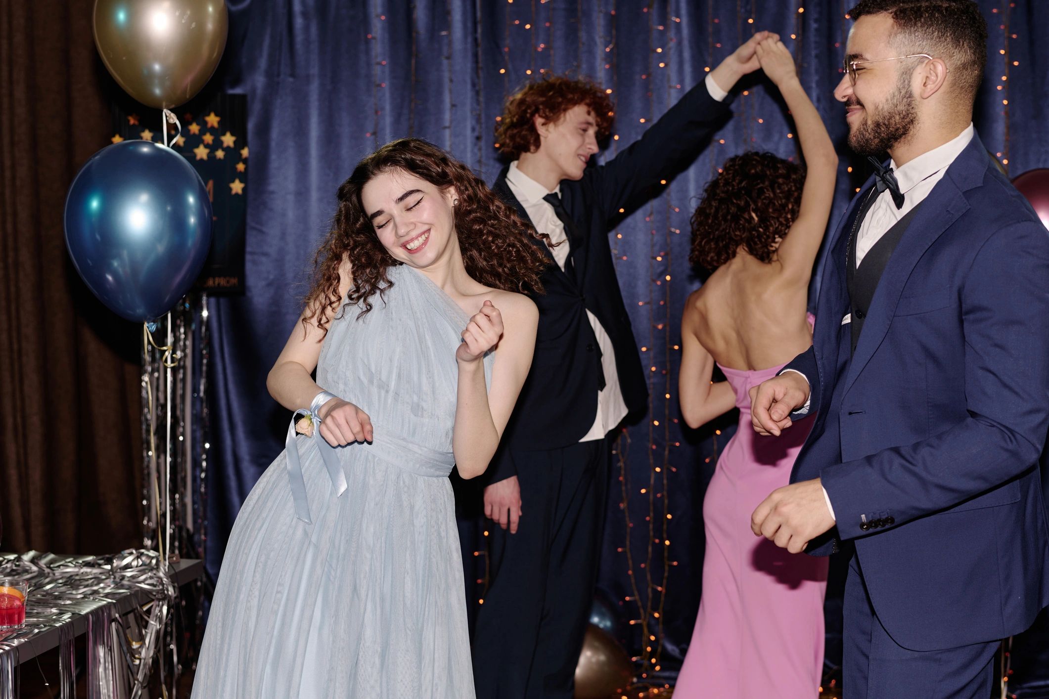 Friends joyfully dancing at a formal party with balloons and festive lights.