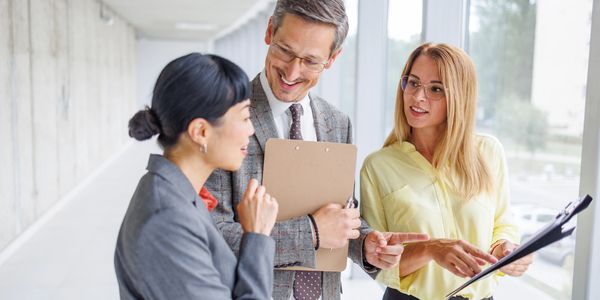 Three professionals discussing documents in a bright office hallway.