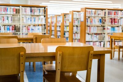Empty wooden tables and chairs in a bright library with bookshelves.