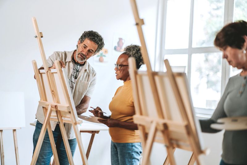Art studio teacher teaches senior students how to paint on canvas
