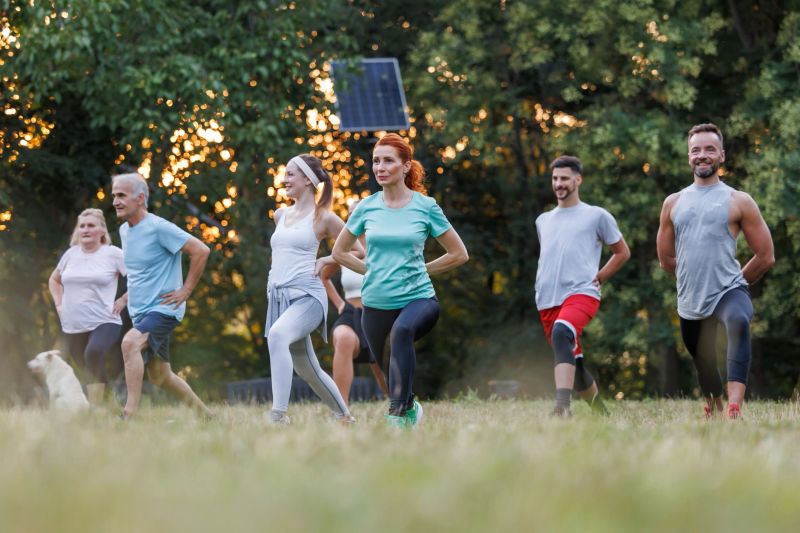 People of various ages and backgrounds perform lunges in a park during sunset. The warm light enhances the energizing atmosphere of the active gathering.