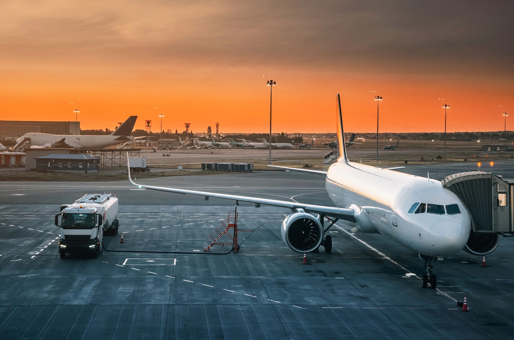 Airplane at the gate during sunset with airport vehicle nearby.