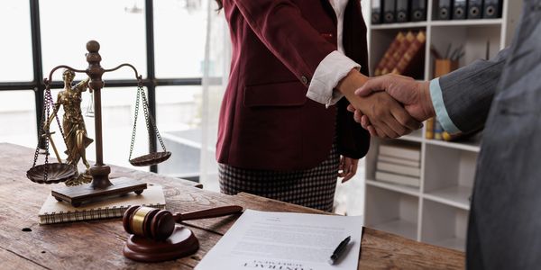 Two professionals shaking hands over a legal contract in an office.