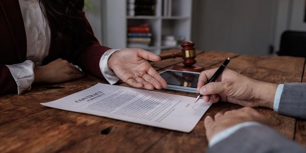 Person signing a contract while another gestures at it.