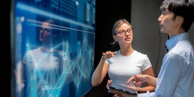 Two professionals discussing data on a digital screen.