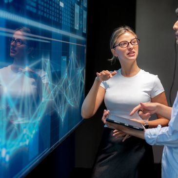 Two professionals discussing data on a digital screen.