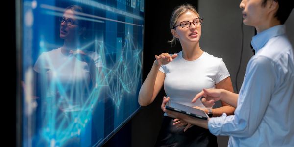 Two professionals discuss data on a digital screen and tablet.