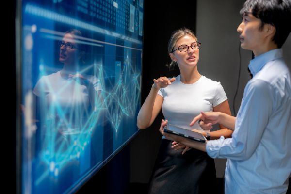 Two professionals discussing data on a digital screen.
