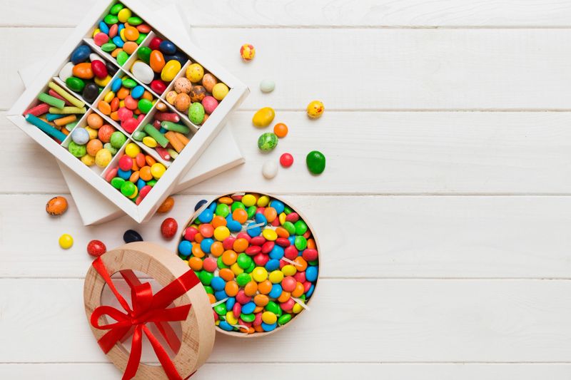 Set of different sweet candy in a paper box with a satin ribbon on a colored background. Holiday concept.