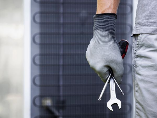 Hand holding wrench and screwdriver, wearing glove.