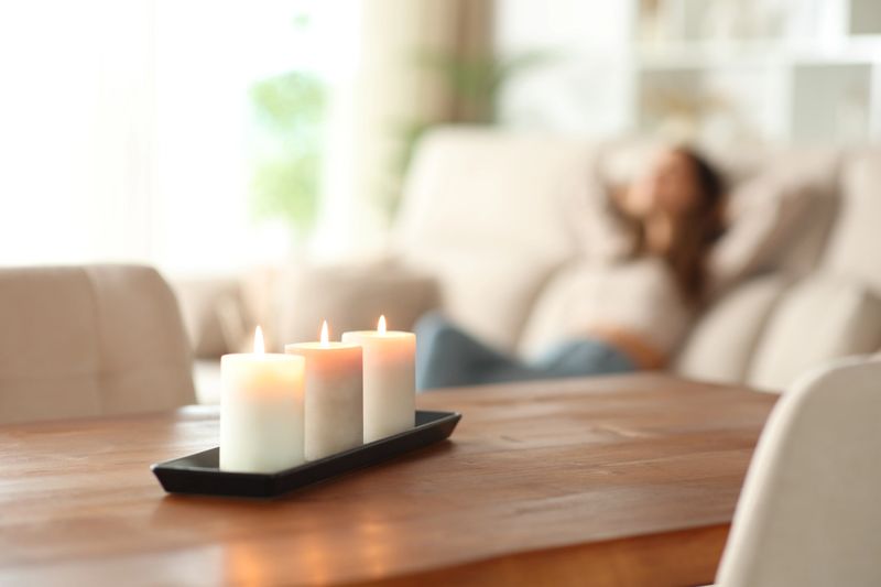 Aromatic candles in foreground and woman relaxing on a couch in the background at home