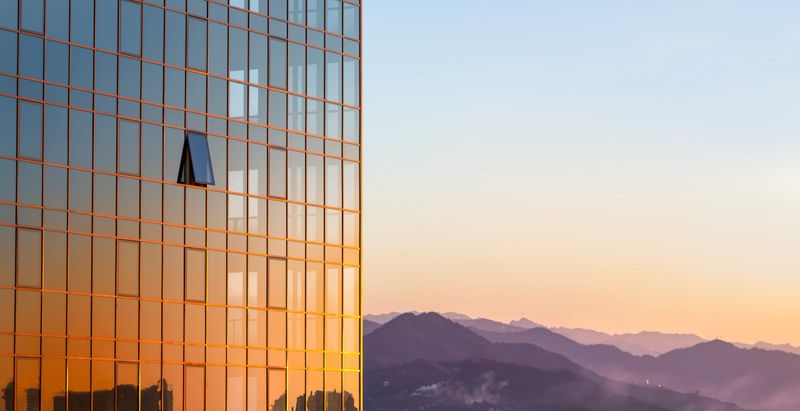 The glass wall of a modern building against the background of the blue- lilac sky and violet mountains in the rays of a golden sunset