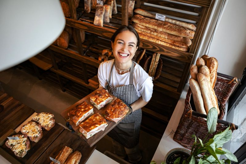 Smiling female baker showing fresh sandwiches in bakery woman holding bread