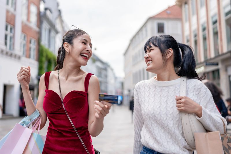 Asian two woman holding shopping bags and walking at outdoors marketplace. Attractive female traveler feel happy and relax, traveling outside department store during holiday vacation trip in Denmark.