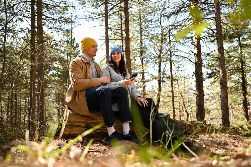 Hikers resting on log and consulting smartphone in forest