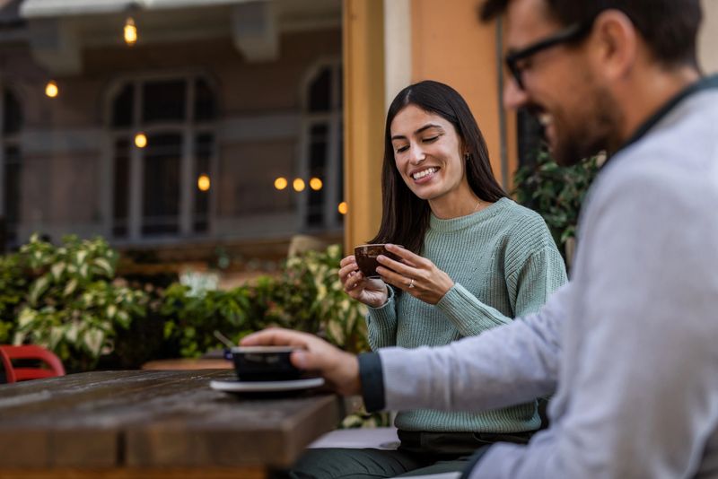 Young couple sitting together at a cozy outdoor cafe, sipping coffee and sharing smiles, enjoying meaningful conversation and creating a warm, inviting atmosphere in the autumn sun