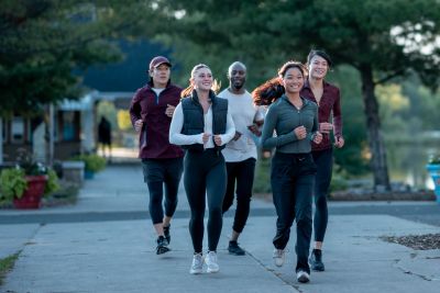 Group of five diverse people jogging outdoors on a paved trail.