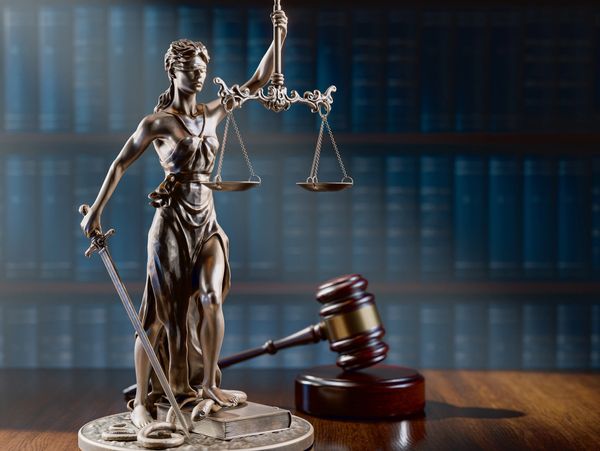 Bronze statue of Lady Justice with scales and sword beside a gavel on a wooden table.