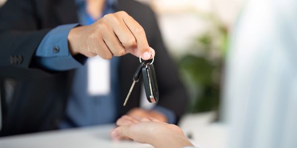 Person handing over car keys to another person in a professional setting.