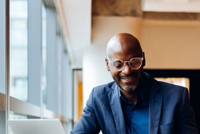 Smiling man in glasses sitting by a window.
