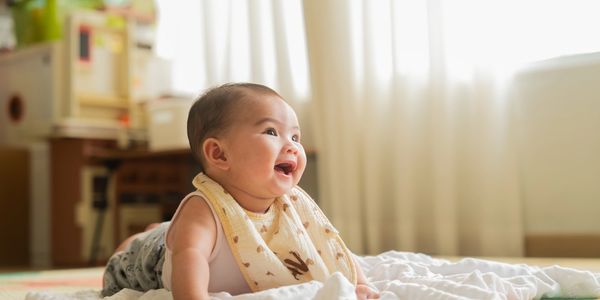 Smiling baby lying on a soft blanket in a sunlit room.