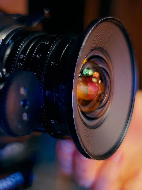 Close-up of a professional video camera lens with controls and a hand adjusting it.