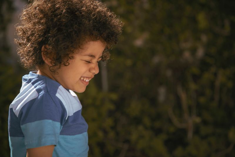 A joyful close-up portrait of a young boy smiling brightly in a garden setting. A heartwarming image full of innocence, happiness, and natural outdoor light.