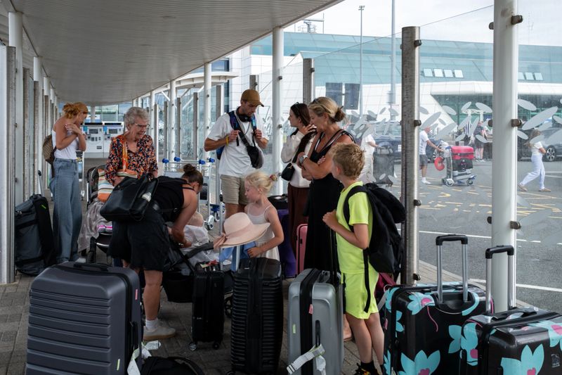 A full shot of a real multigenerational family standing with their suitcases outside an airport. They are all wearing summer clothing, talking together next to their suitcases. Located in Newcastle Upon Tyne