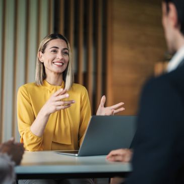 Smiling woman in yellow blouse discussing with colleagues at a meeting.