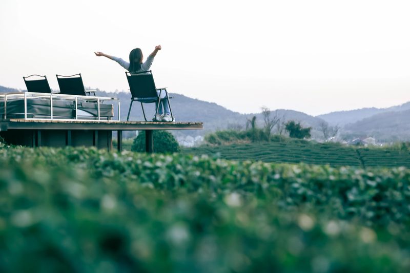 Asian woman with her back to the camera, embracing the sunset with her hands on the top of a mountain