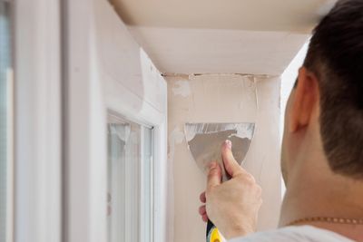 Man smoothing plaster on wall corner with putty knife.
