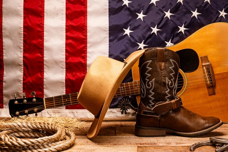 Country themed Americana setting of a rustic western scene featuring an American flag, cowboy hat, guitar, horseshoes, and cowboy rope. The arrangement conveys themes of patriotism, Americana, and cowboy lifestyle, making it ideal for western culture, tradition, and rustic concepts.