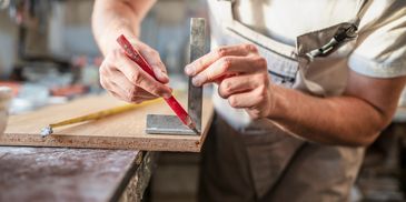A carpenter marking wood with a pencil and square tool.