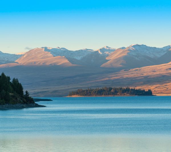 A serene landscape featuring rolling hills, a calm lake, and a clear blue sky with a few fluffy clouds.