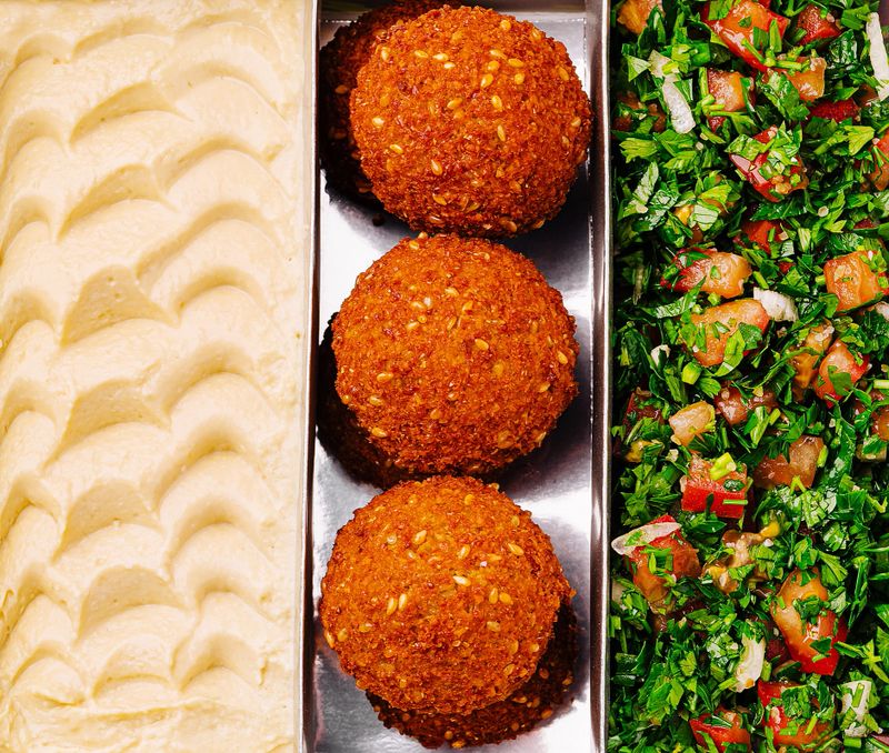A vibrant lunch spread features golden falafel balls, fresh diced salad, and smooth, creamy dip. Bright colors and textures highlight the delicious Middle Eastern flavors enjoyed together.