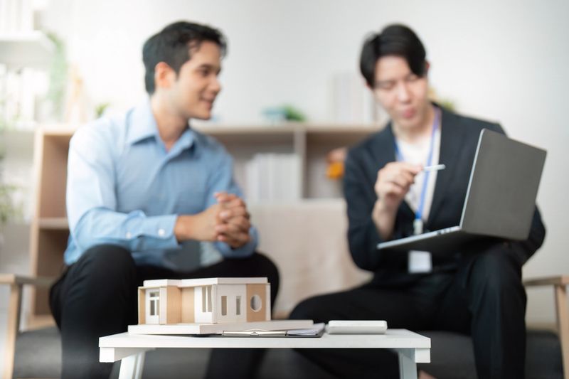 Two men engaged in a real estate consultation, analyzing a model house while discussing property details in a modern office.